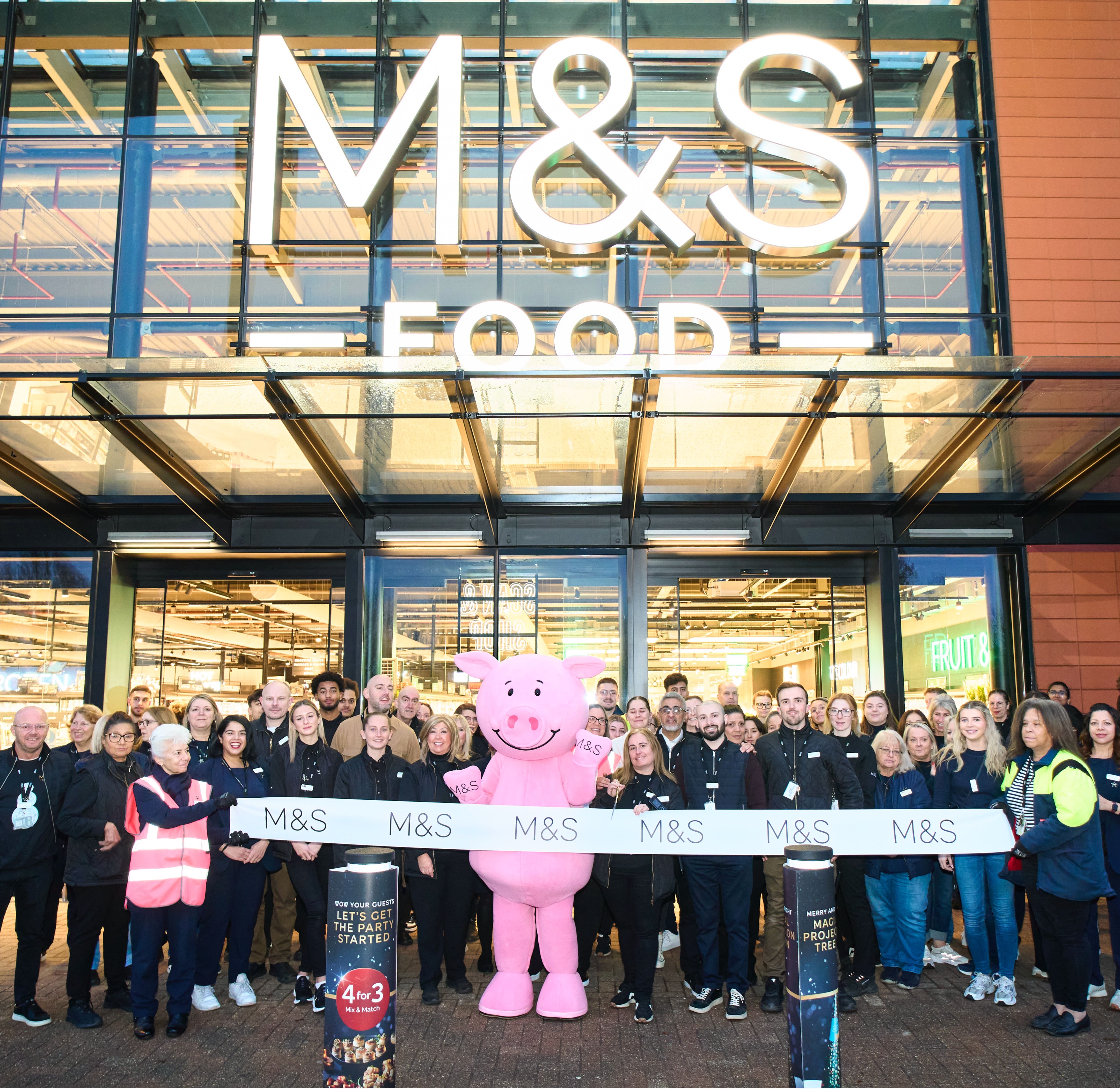 a group of people standing outside an M&S store about to cut the ribbon for the opening